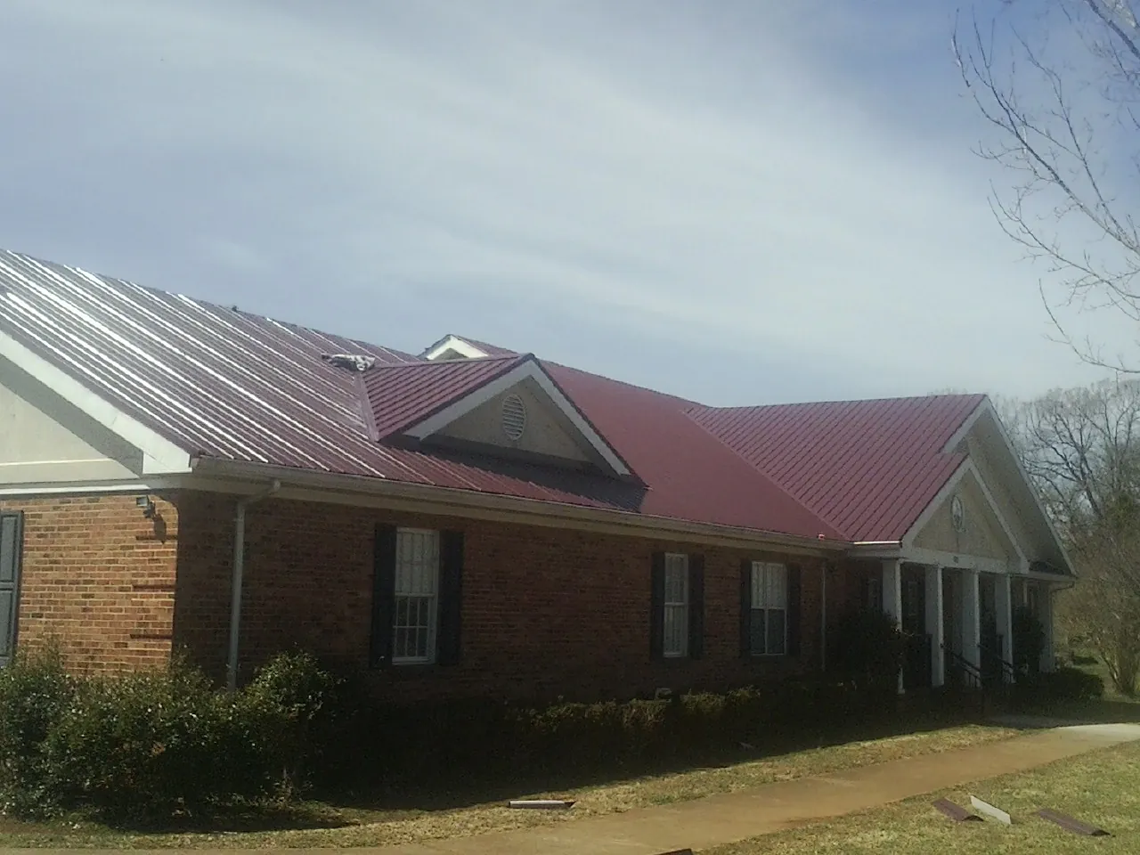 Red metal roof with gabled entries on a long brick building, from a Hail Damage Roof Repair job in Garards Fort