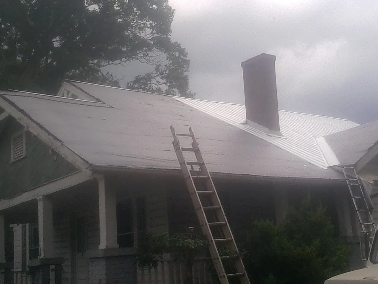 Ladders against a metal roof on an older home with a brick chimney in Garards Fort