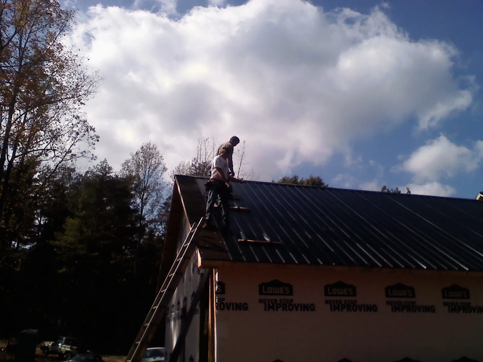 Roofer fastening dark metal panels high against a cloudy sky, from a Roof Inspection job in Garards Fort
