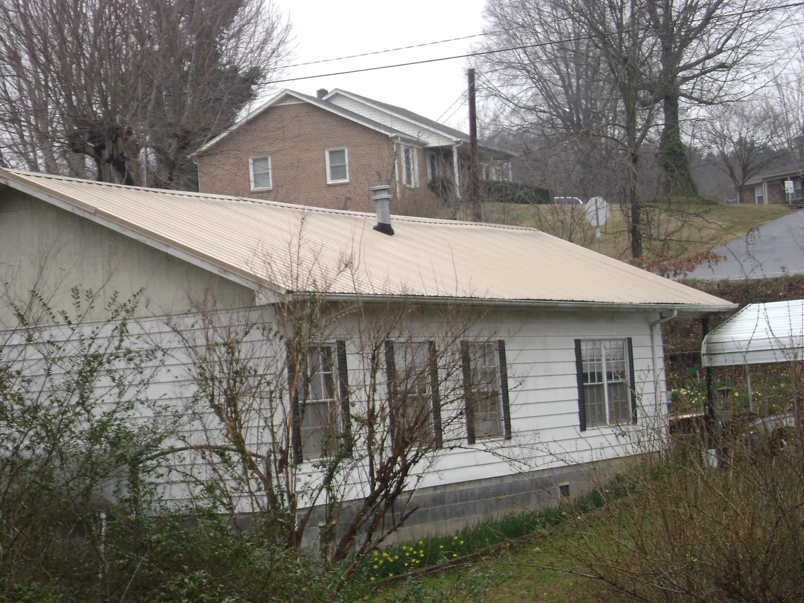Tan metal roof on a white sided house set into a hillside — Commercial Roofing by Roofing Brothers in Garards Fort